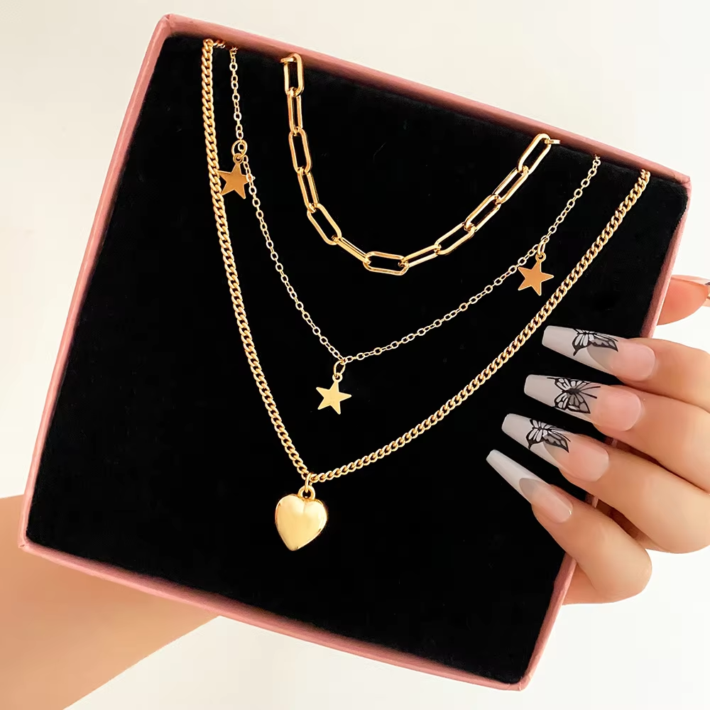 Gold necklaces with star and heart pendants on a black display stand, held by a hand.