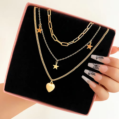 Gold necklaces with star and heart pendants on a black display stand, held by a hand.