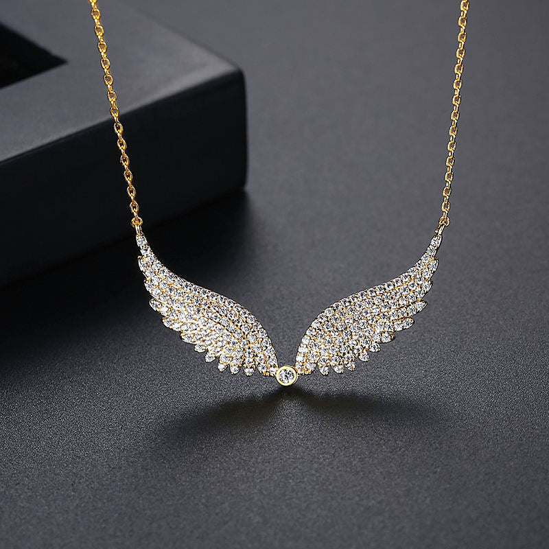 Gold necklace with angel wing design on a dark surface