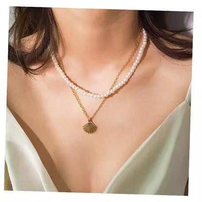 A close-up of a model wearing a double-strand necklace featuring white pearl beads and a gold chain with a gold shell pendant.
