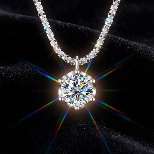 A silver-tone necklace with a large round brilliant-cut clear gemstone pendant, displayed on a black velvet background with rainbow light flares.
