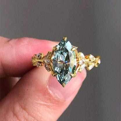 Gold ring with a large green gemstone held between fingers against a dark background