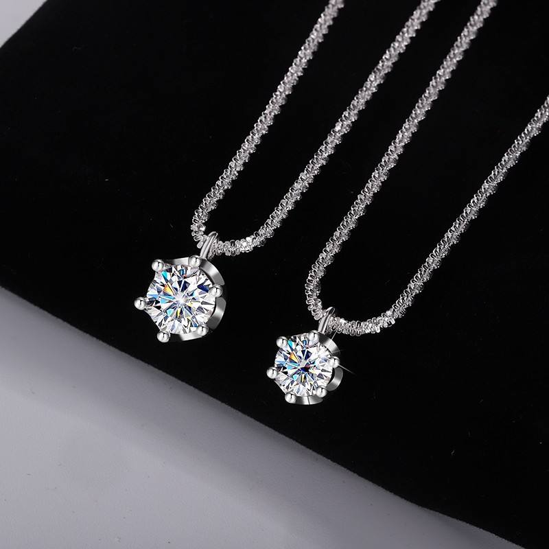 Two silver-toned necklace pendants with round clear gemstones on textured chains, displayed on a black background with a white corner visible.