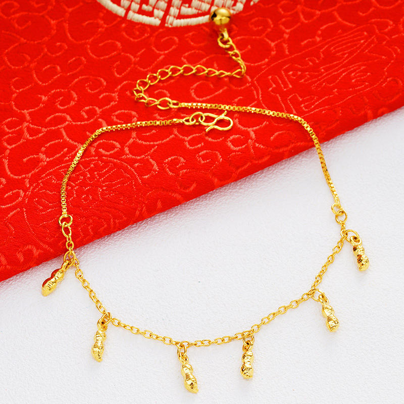 A delicate gold chain anklet with five dangling textured charms, displayed on a split white and red background.