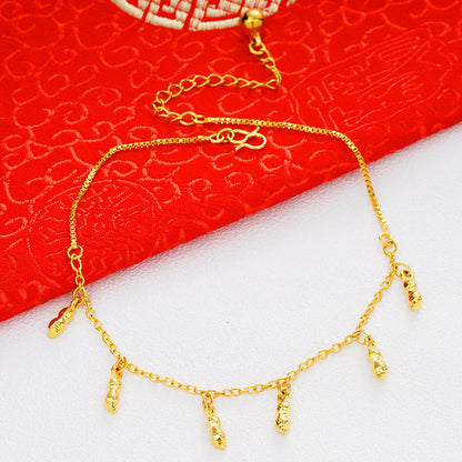 A delicate gold chain anklet with five dangling textured charms, displayed on a split white and red background.
