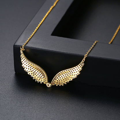 Gold angel wings pendant necklace on a matching chain, displayed on a black jewelry box against a dark gray background.